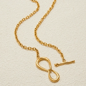 Collier en acier inoxydable doré avec pendentif infini et fermoir OT sur fond beige