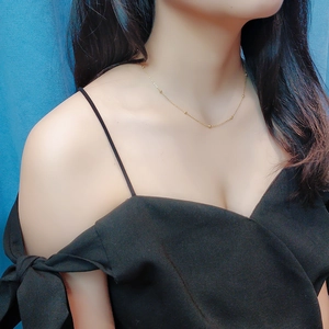 Détail d'un collier à billes dorées minimaliste porté par un mannequin sur noir