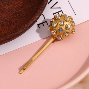 Detail shot of a golden ball hair clip with sparkling white rhinestones on pink background