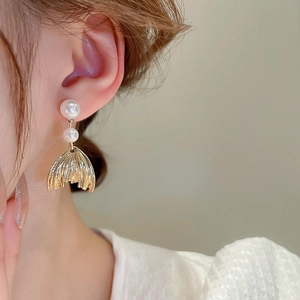 Close-up of golden fishtail pendant earrings with white imitation pearls for women