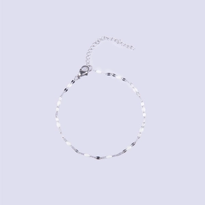 Detailed macro view of thin silver chain bracelet with white enamel oval accents and clasp