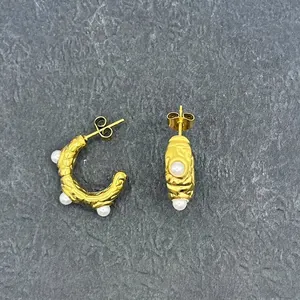 Detailed view of C-shaped gold textured earrings with small pearls on stone background