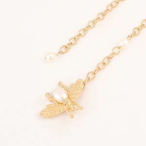 Close-up of golden metal waist chain featuring pearl accents and a bee charm