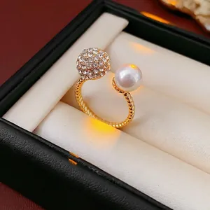 Elegant gold twisted open ring with a white pearl and a pave crystal ball in a jewelry box