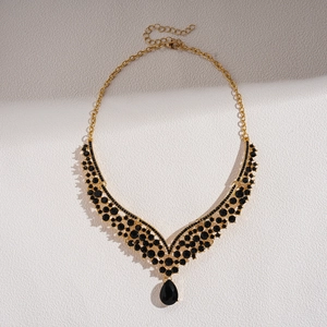 Detail of V-shaped gold necklace with black round and teardrop rhinestones on white