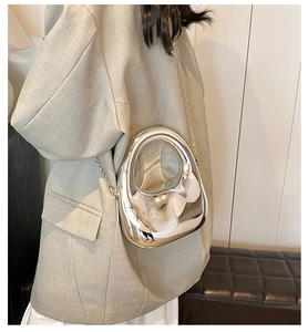 Irregular oval silver acrylic clutch bag with metal chain shown on model's shoulder