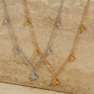 Elegante Schmetterlingshalsketten aus Edelstahl in Gold und Silber auf beigem Marmor