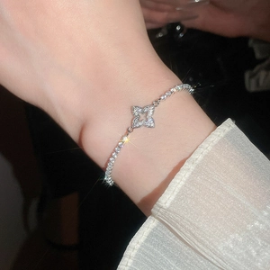 Detail of a sparkling silver bracelet featuring a hollow clover pendant worn on wrist