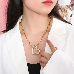 Close-up of a gold-colored beaded chain with a crystal heart pendant on a model