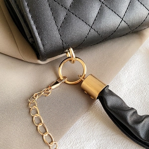 Detalle de bolso acolchado negro con anillas metálicas doradas y adorno de borla