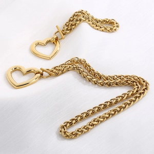 Close-up of golden braided dragon bone chains with heart-shaped clasps on textured fabric