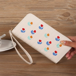 Detail of cream-colored long wallet with floral embroidery and gold zipper closure