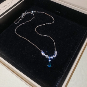 Macro detail of silver drop necklace with blue gemstone and zircon on black velvet