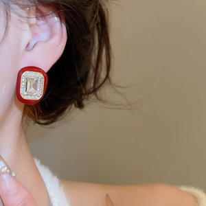 Macro view of gold square earring with red enamel and emerald cut crystal on ear