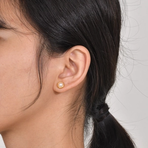 Close-up of a minimalist round pearl earring with gold border worn on ear