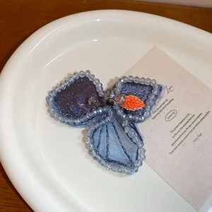Close-up of handmade floral hair clip with blue beads and orange leaf detail