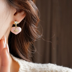 Close-up of heart earrings with a clear gemstone stud and a pink heart-shaped pendant