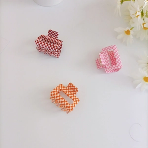 Close-up of small checkered square hair claws in red, orange, and pink acrylic material