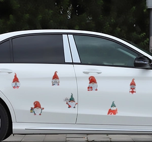Detail of seven Christmas gnome magnetic stickers on a white car door with Merry Christmas signs