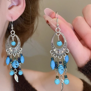 Close-up of bohemian turquoise drop earrings with silver leaf tassels and beaded detail