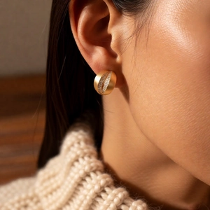 Detail of C-shaped matte gold stud earrings with cubic zirconia inlay on model ear