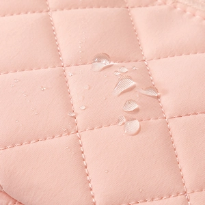 Macro view of pink quilted fabric with water droplets highlighting waterproof quality