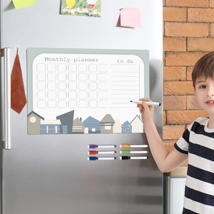 Close-up of a magnetic monthly planner on a fridge with a child writing on it