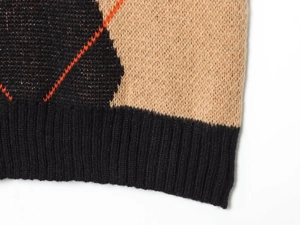 Detail of diamond pattern knit vest with black, beige, and orange ribbed hemline