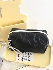 Detail of black quilted bow makeup bag with white zipper and pearl heart pendant charm