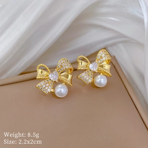 Close-up of bow earrings with heart zircon and pearl on a jewelry box edge
