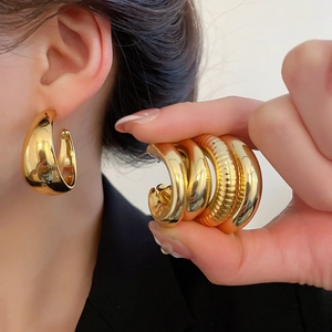Detail of model wearing chunky gold hoop earrings with smooth and ribbed metal textures