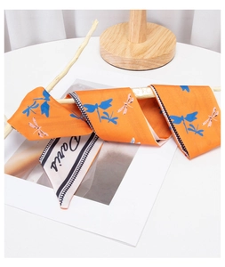 Detail of orange dragonfly print silk scarf tied on wood for French style styling