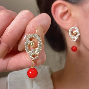 Detail of gold snake earrings with white crystals and a vibrant red round bead drop