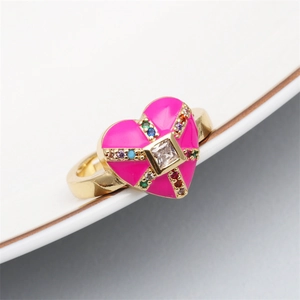 Close-up of gold heart ring with pink enamel and colorful zircon stones on ceramic