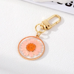 Detail of a golden keychain with a pink dried daisy flower resin pendant charm