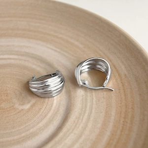 Detail shot of silver metallic earrings featuring unique wave texture on minimalist wood