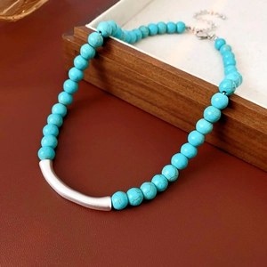 Vue détaillée du collier de perles turquoise avec tube argenté sur un plateau de présentation