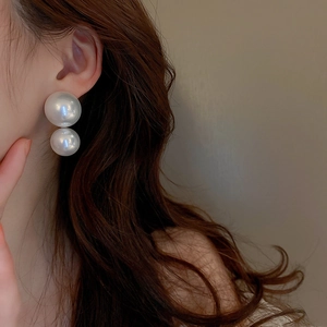 Close-up of minimalist large double pearl earrings worn by a model in warm light