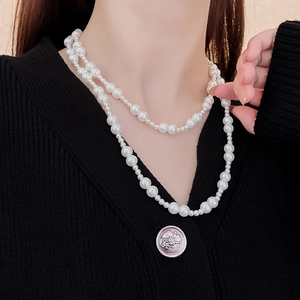 Détail d'un collier de perles blanches à double rangée avec fermoir OT sur pull noir