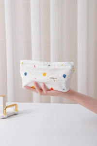 Detail of white cotton cosmetic bag featuring colorful embroidered dots and fabric logo label