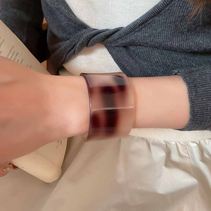 Close-up of a brown amber acetate open bangle worn by a woman with a cozy book setting
