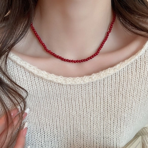 Close-up of minimalist red glass beaded necklace on model with white knit sweater