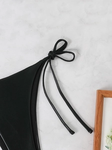 Detail of black matte leather-like bikini with delicate lace-up bow on marble surface