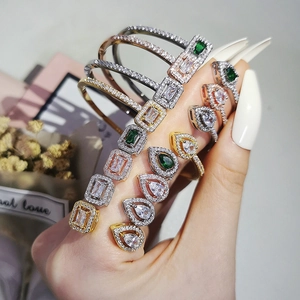 Close-up of gold, silver, and rose gold bracelets set with marquise-cut green and white cubic zirconia