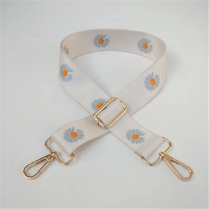 Detail view of beige canvas shoulder strap with blue daisy print and gold metal buckles