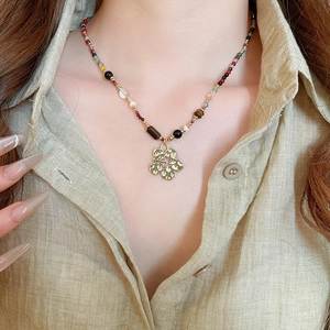 Close-up of bohemian beaded necklace with golden flower pendant on model neckline