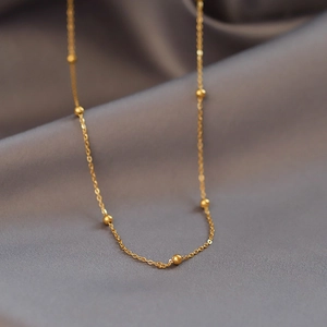 Gros plan d'un collier chaîne à perles dorées minimaliste sur du satin gris doux