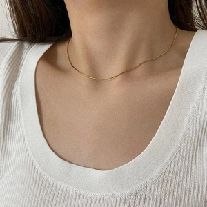 Detail of ultra-thin minimalist gold necklace worn on neck with white knitted top