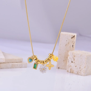 Close-up of golden snake chain necklace with daisy and turquoise heart charms on stones