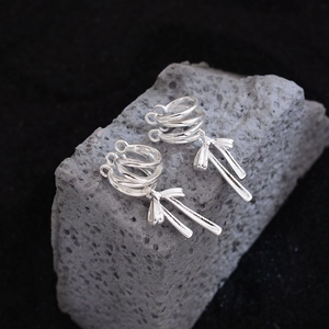 Elegant silver ribbon bow ear cuffs with long metal tassels on a textured grey stone base